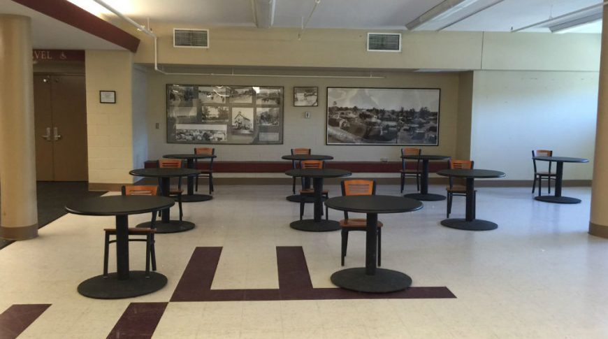 Interior open area with small round black tables with chair at each with two large black and white photos to the back wall.