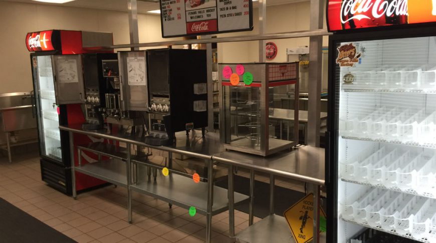 Cafeteria stainless steel tables with drink machines and pop vending machines on either side.