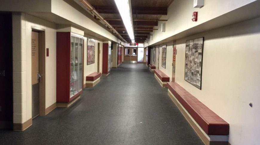 Long hallway with built-in bench seating with maroon vinyl seats on either wall and showcase glass cabinetry with sports memorabilia throughout.