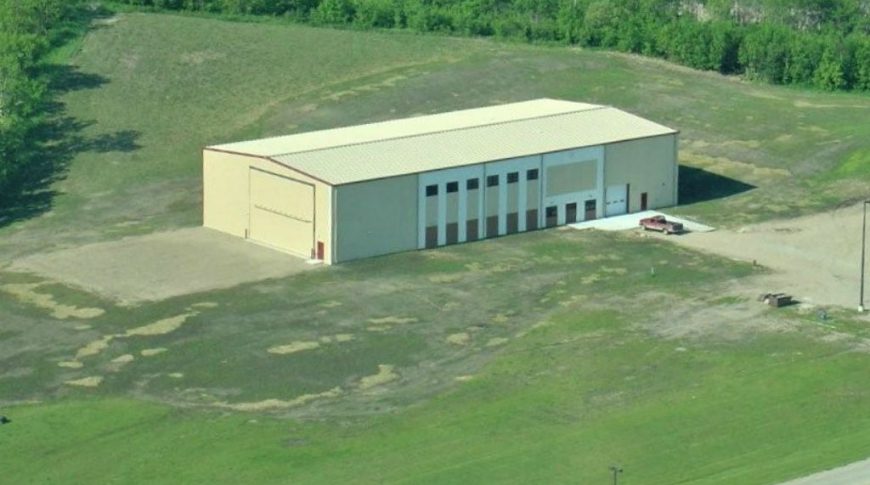 Aerial view of large beige rectangular building with green grass and trees on each side.