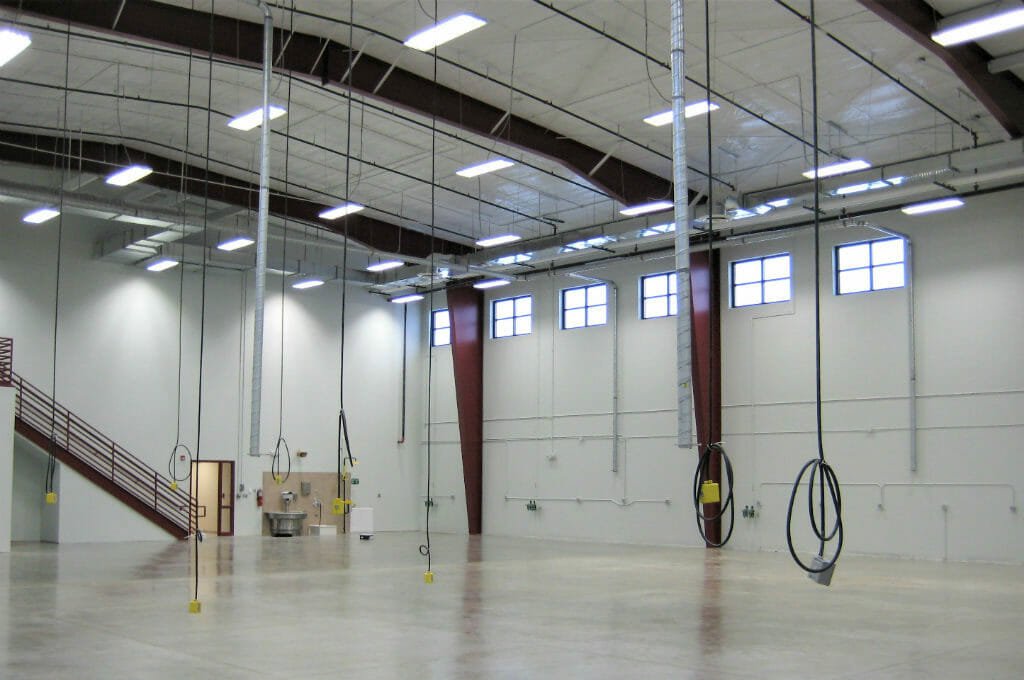 Large two-story open workshop area with cords hanging from ceiling and concrete flooring.