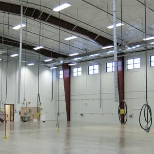 Large two-story open workshop area with cords hanging from ceiling and concrete flooring.