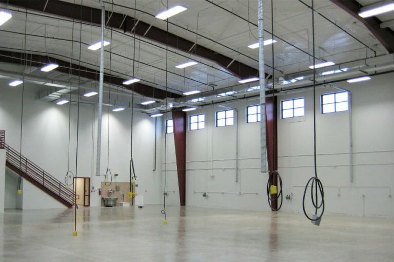 Large two-story open workshop area with cords hanging from ceiling and concrete flooring.