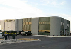 Precast concrete and dark green siding accent two-story office building with sign saying "Comstock" on boulevard.
