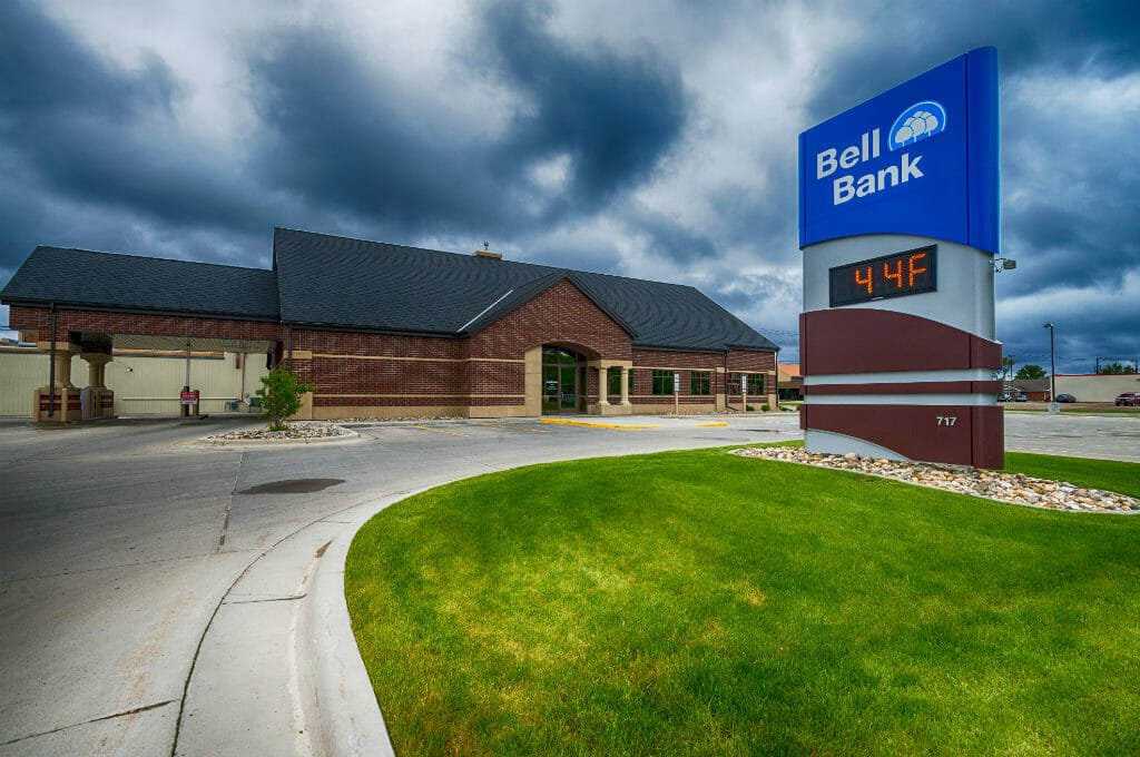 Exterior view of dark red bricked building with digital sign in foreground with "Bell Bank" logo on blue background.