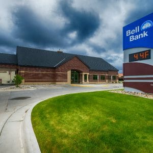 Exterior view of dark red bricked building with digital sign in foreground with "Bell Bank" logo on blue background.