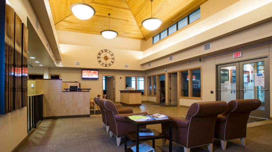 two-story interior room with light wood paneled ceiling with beige walls and dark brown chairs beneath.