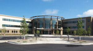 Front view of a large three-story beige brick and light paneled building with curved entrance with all three stories of windows.