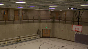 Concrete brick walled gymnasium viewed from second story running track looking down at the basketball court and three row retractable bleachers.