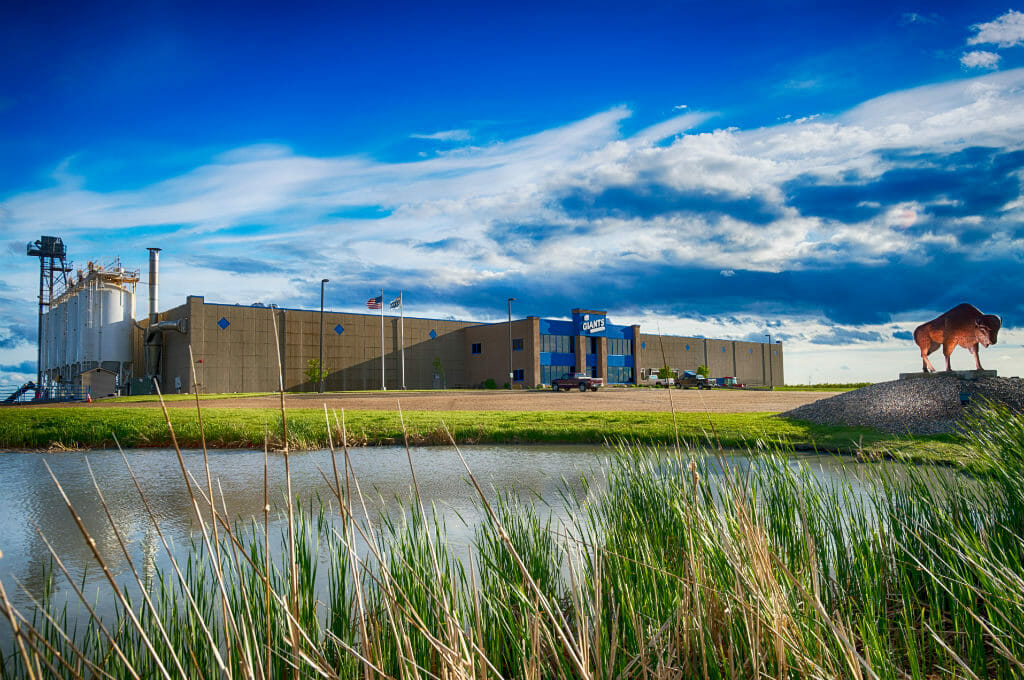 Exterior view of brown and blue precast concrete warehouse building with buffalo statue to right and pond in foreground.