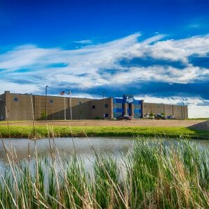 Exterior view of brown and blue precast concrete warehouse building with buffalo statue to right and pond in foreground.