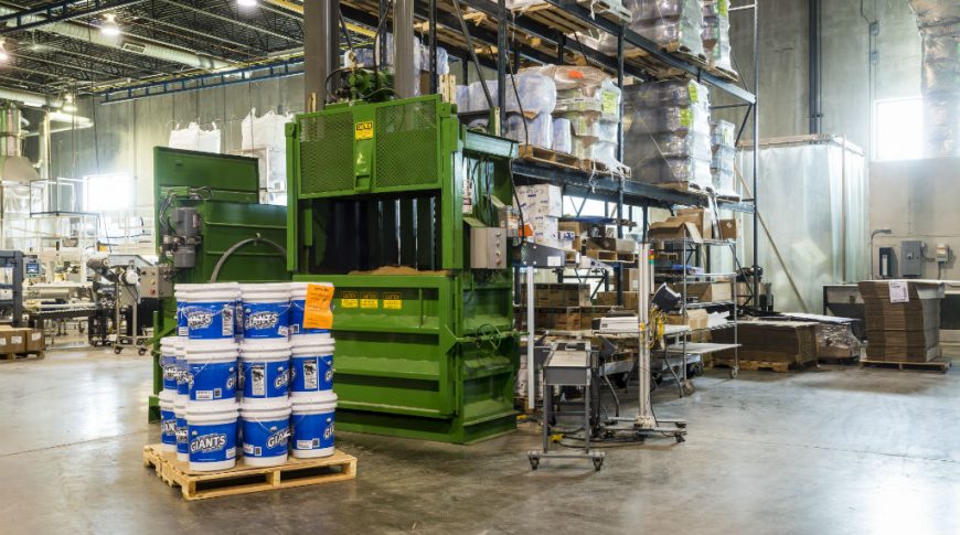 Concrete-floor factory with green machinery in foreground with pallet racks throughout.