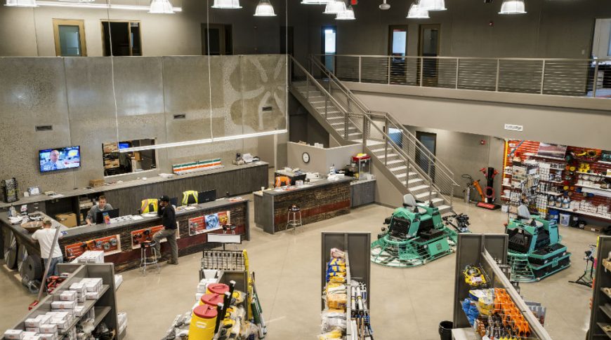 Interior view from second floor mezzanine of supply store interior with rows of supplies to bottom and reception desk to back.