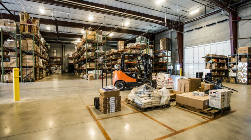 Warehouse with concrete floors, metal roof, and precast concrete exterior walls. Rows of 4-stacked high pallet storage racks.