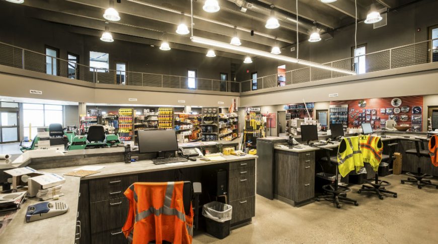View from back of reception desks to see rows of supply shelves behind with second floor mezzanine above.