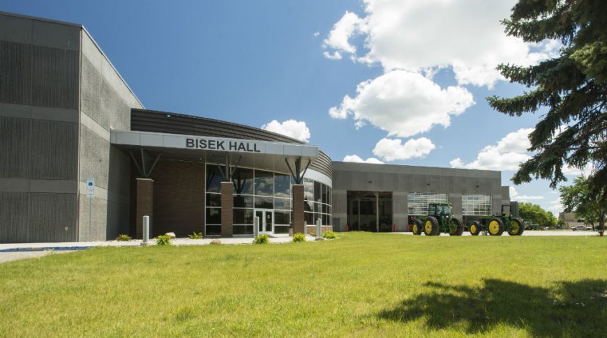 NDSCS Bisek Hall-P-Ext1-1024x680-Education Construction Front view of outside entrance to Bisek Hall precast concrete building with brick rotunda and floor-to-ceiling windows.