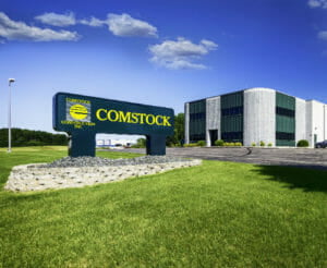 Comstock Construction precast concrete building in Fergus Falls, MN with dark green panels with Comstock sign in the foreground and bright blue sky with clouds in the background.