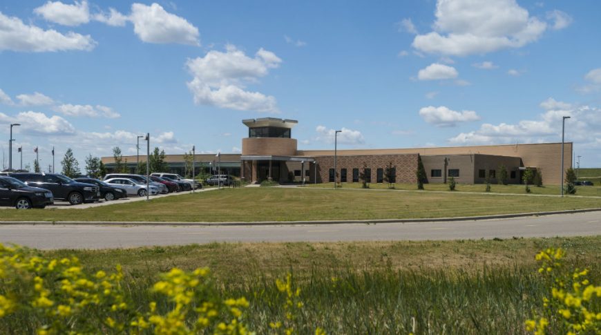Exterior view across the street of brick and precast concrete building with round rotunda extending to second story hovering above the rest of the building. Parking lot to the far left and grassy area in front with street in foreground.