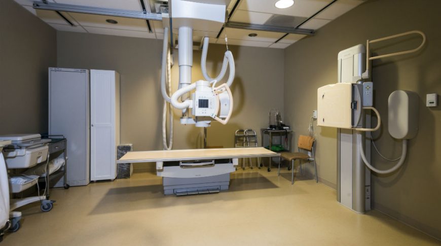Interior view of imaging room with x-ray table and stand with beige floor and taupe walls.