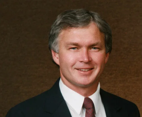 LeMar_Lynn-Bob-cropped-500x410 Middle-aged man with salt and pepper hair wearing black suite, white button-up and red speckled tie on brown backdrop