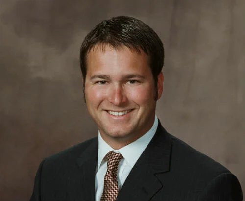 LeMar_Michael-500x410 White man with short brown hair and brown eyes wearing a black suite with white collared shirt and red geometric tie on brown background