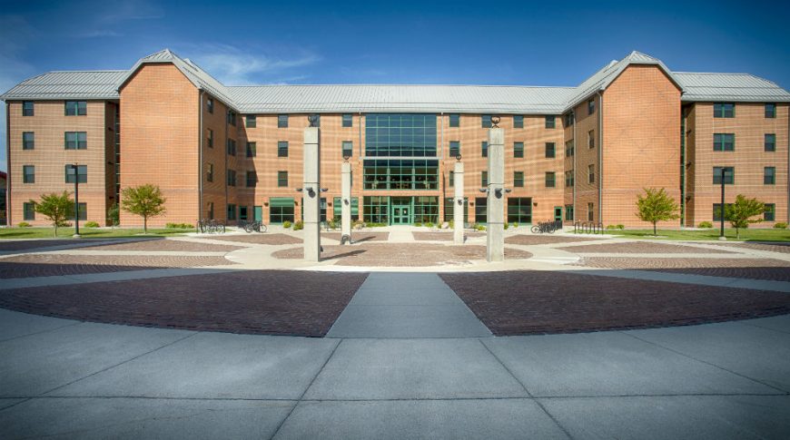 Front of large 4-story learning living college center building with brown brick and concrete walkways in foreground.