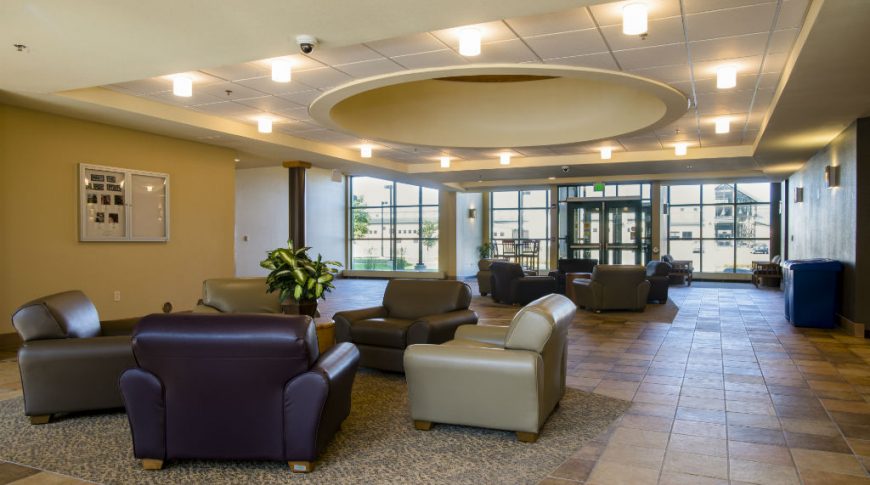 Large entryway with shades of brown tiles and two carpeted seating area with chairs and center table, one in foreground and one in the background.