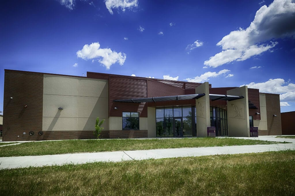 Exterior brown brick and beige concrete school building with a few large rectangular entryway divider columns with eagle emblems etched on the concrete.