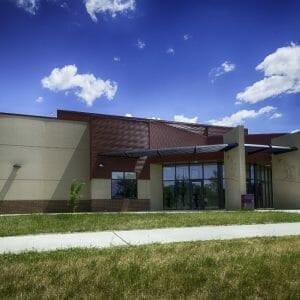 Exterior brown brick and beige concrete school building with a few large rectangular entryway divider columns with eagle emblems etched on the concrete.