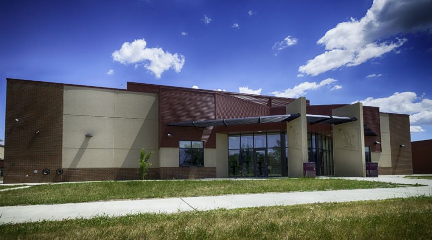 Exterior brown brick and beige concrete school building with a few large rectangular entryway divider columns with eagle emblems etched on the concrete.