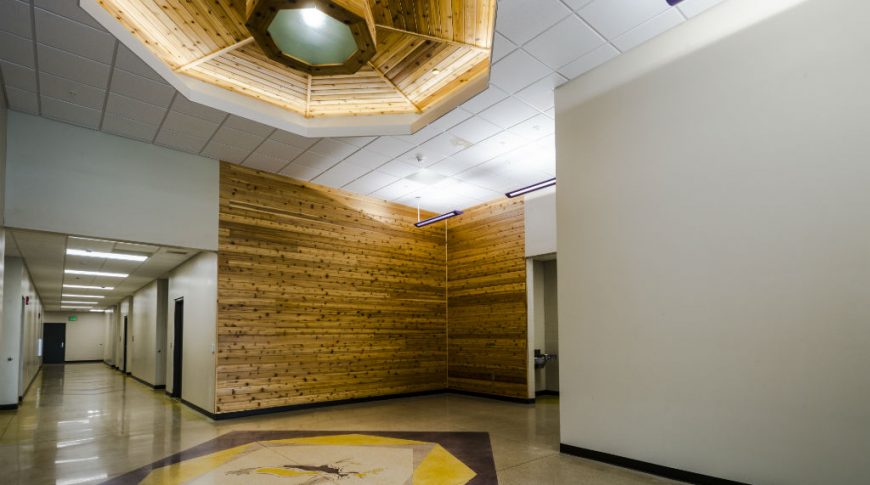 Interior corridor of New Town school with wooden paneled accent walls and overhead decagon-shaped paneled alcove with skylight in the middle. Beneath is an eagle emblem with purple and yellow school colors outlining it.