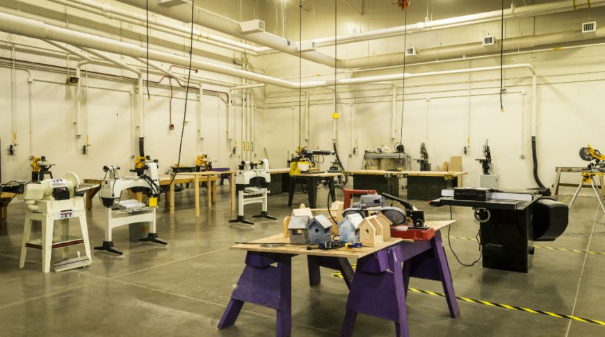 Large workshop with high ceilings with outlets hanging down and workstations with saws throughout.