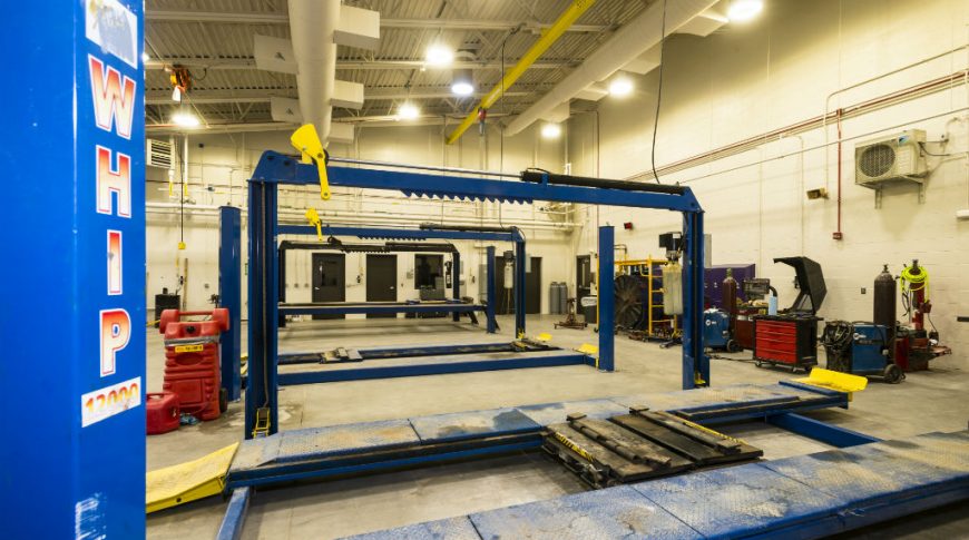 Light tan painted cinder-block room with mechanic equipment and vehicle lift stations throughout.