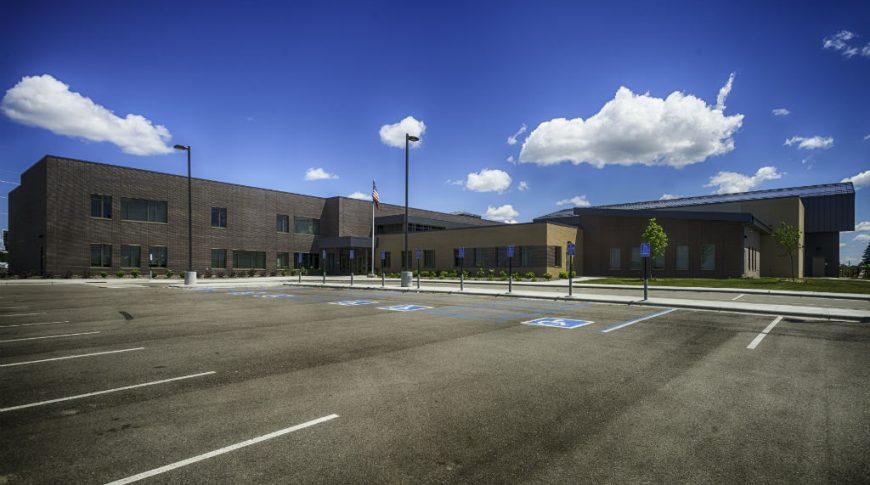 Exterior view of dark brown brick school with American flagpole in center by entrances.