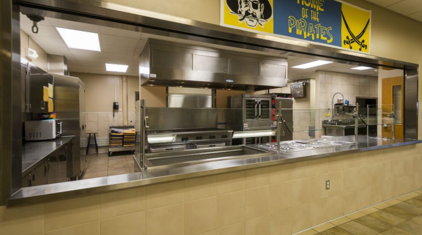 Tioga High School-P-Int3-1024x680-Education Construction Cafeteria passthrough wall with stainless steel surround and stainless steel kitchen equipment and appliances in the back.