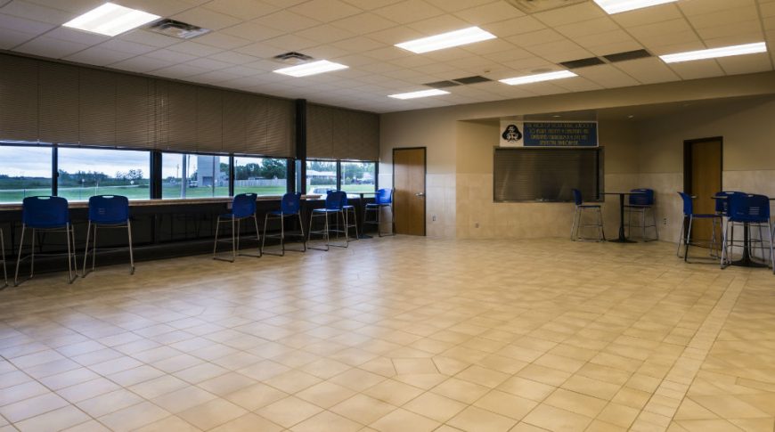 Tioga High School-P-Int4-1024x680-Education Construction Large tiled cafeteria space with back wall of bar height counter and chairs facing outward toward windows.
