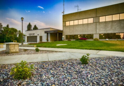Exterior view of the Bottineau County Jail entrance. Features a precast concrete exterior with green lawn in front of the entrance and rock and sidewalk landscaping to the foreground