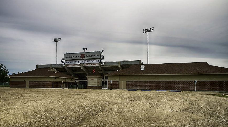 Back side of concrete stadium with brick building and parking lot beneath