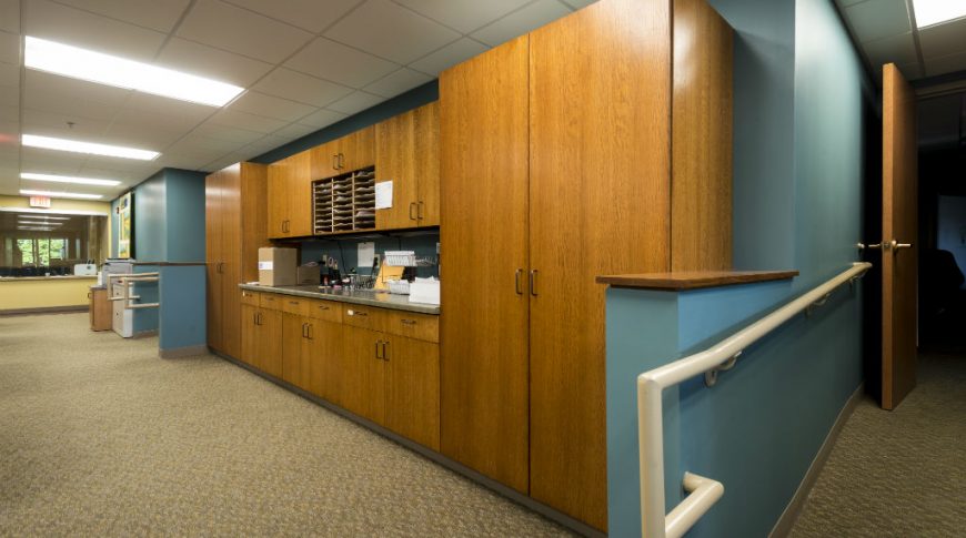 OtterTail Courthouse-P-Int2-1024x680-Government Construction Wooden cabinetry with blue accent walls on either side, brown carpet below and fluorescent lights on paneled ceiling above