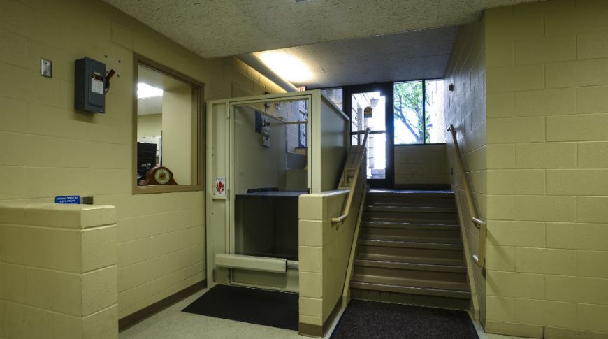 OtterTail Courthouse-P-Int5-1024x680-Government Construction Wheelchair lift just to the inside of the courthouse side entrance surrounding by beige cinder-block walls and stairwell