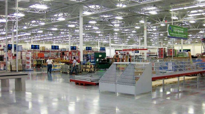 Front entry view of inside of super store with fluorescent and skylights above, concrete floors below and merchandise wracks throughout.