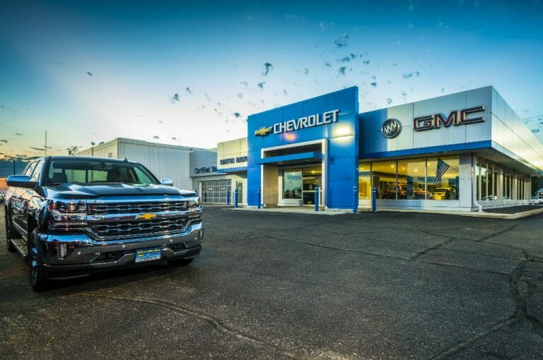 Parking lot angled view of Smith Motors gray and blue building with shiny truck to the foreground