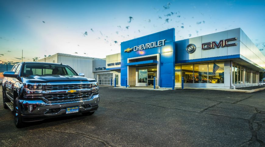 Parking lot angled view of Smith Motors gray and blue building with shiny truck to the foreground