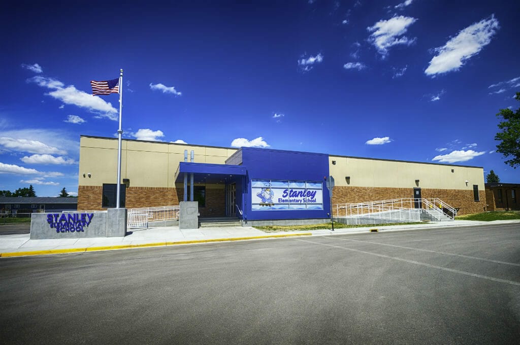 Exterior parking lot view of brown and beige concrete school entrance with bright blue bump-out entrance and flagpole to the left