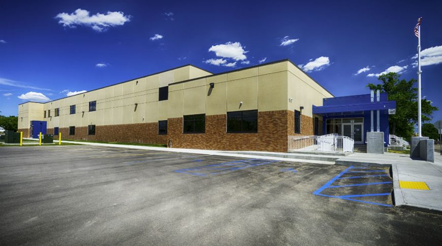 Stanley Elementary School-P-Ext2-1024x680-Education Construction Exterior parking lot view of brown brick lower and light beige precast concrete upper walls with bright blue accented entrance.