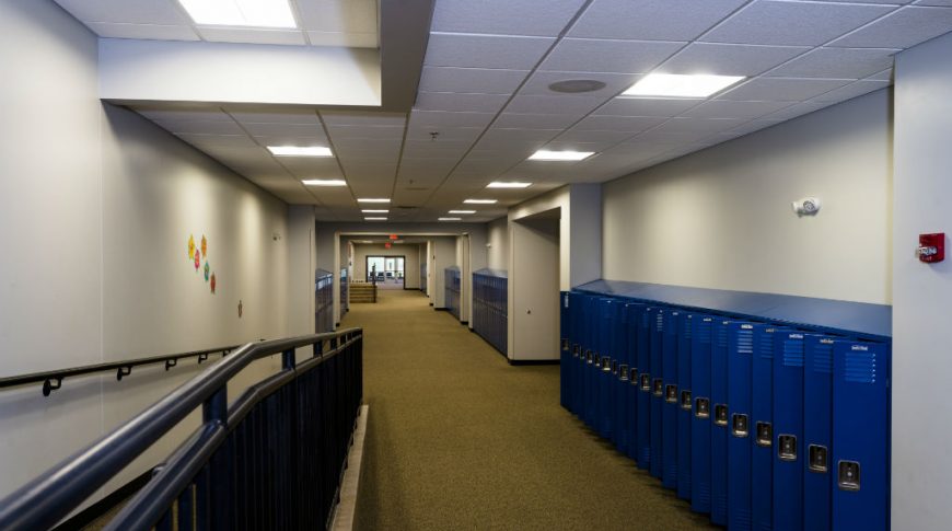 Stanley Elementary School-P-Int4-1024x680-Education Construction Long hallway of bright blue lockers with light gray walls and ceiling tiles above with brown speckled carpet beneath. and a wheelchair ramp to the left side.