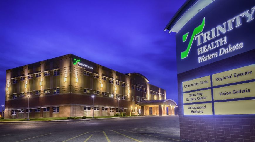 Trinity Health Western Dakota-P-Ext1-1024x680-Healthcare Construction Exterior view of Trinity Health Center in Williston, ND showcasing lit up brown brick façade at dusk with lit up sign to the right in the foreground