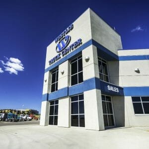 Up-close view of the front outside entrance of the Westlie Truck Center precast beige building with blue stripes in the middle and top with their sign on the top