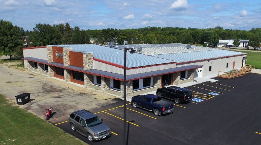 Aerial corner view of Tag Up beige and white metal building with metal silver roof, red gutters and brown accent panels.