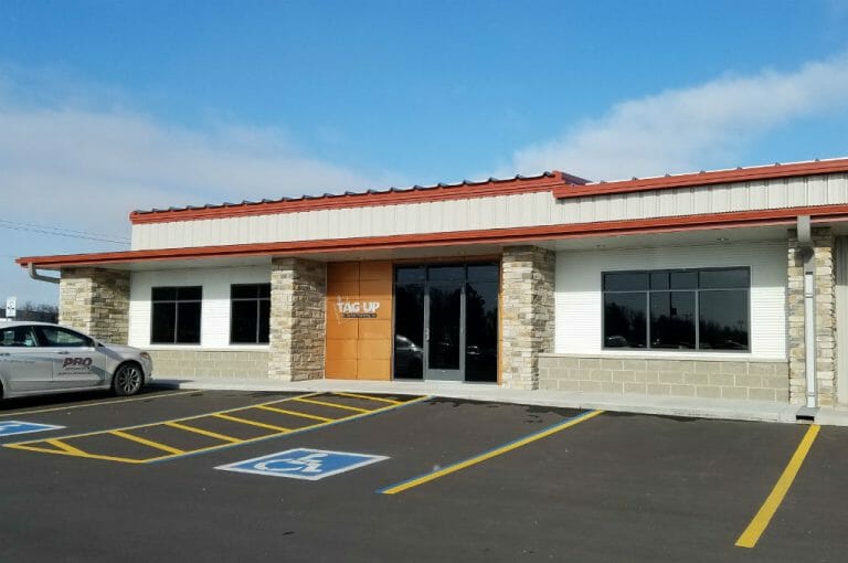 Entrance of beige and white metal building with brickwork columns and red gutters with brown panel accents.